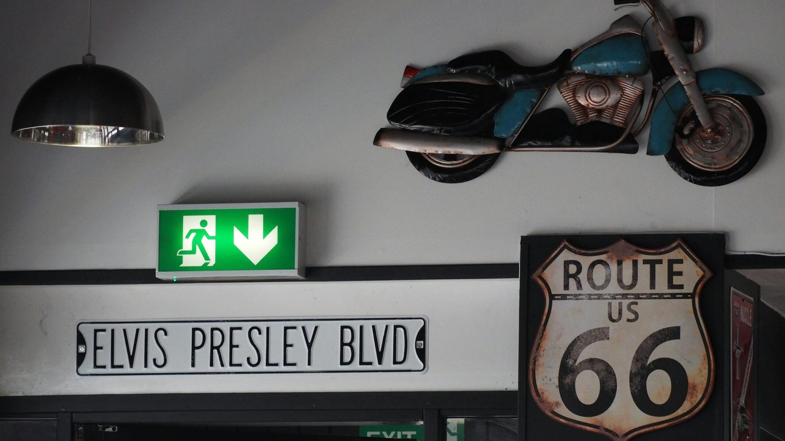 A wall displaying various items of American cultural significance, including an exit sign, a sign stating "Elvis Presley Blvd," a motorcycle, and a sign stating "Route US 66."